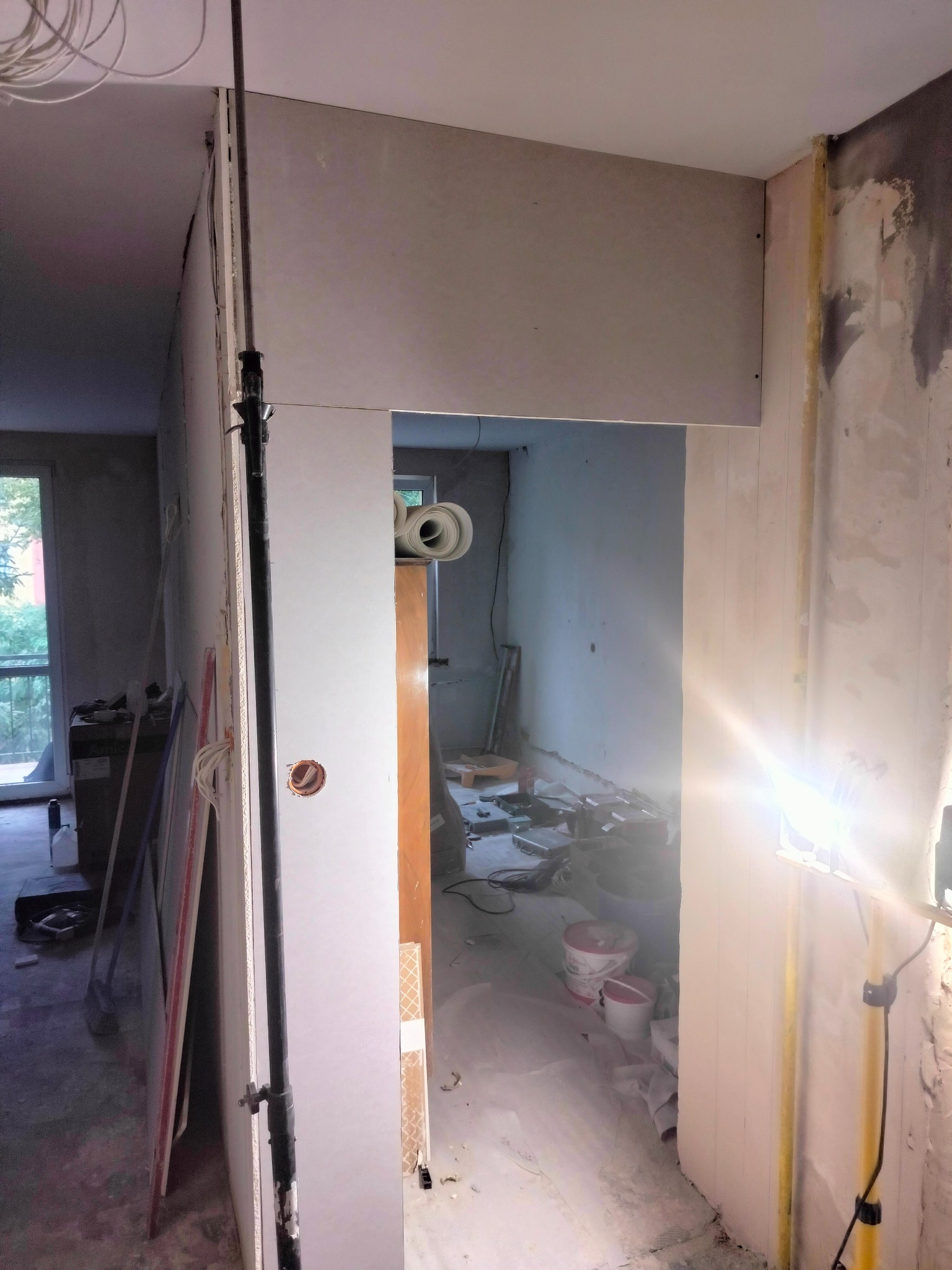 Wnętrze w trakcie montażu płyt gipsowo-kartonowych, widoczny profil pionowy, przewody elektryczne i prowizoryczne oświetlenie halogenowe.