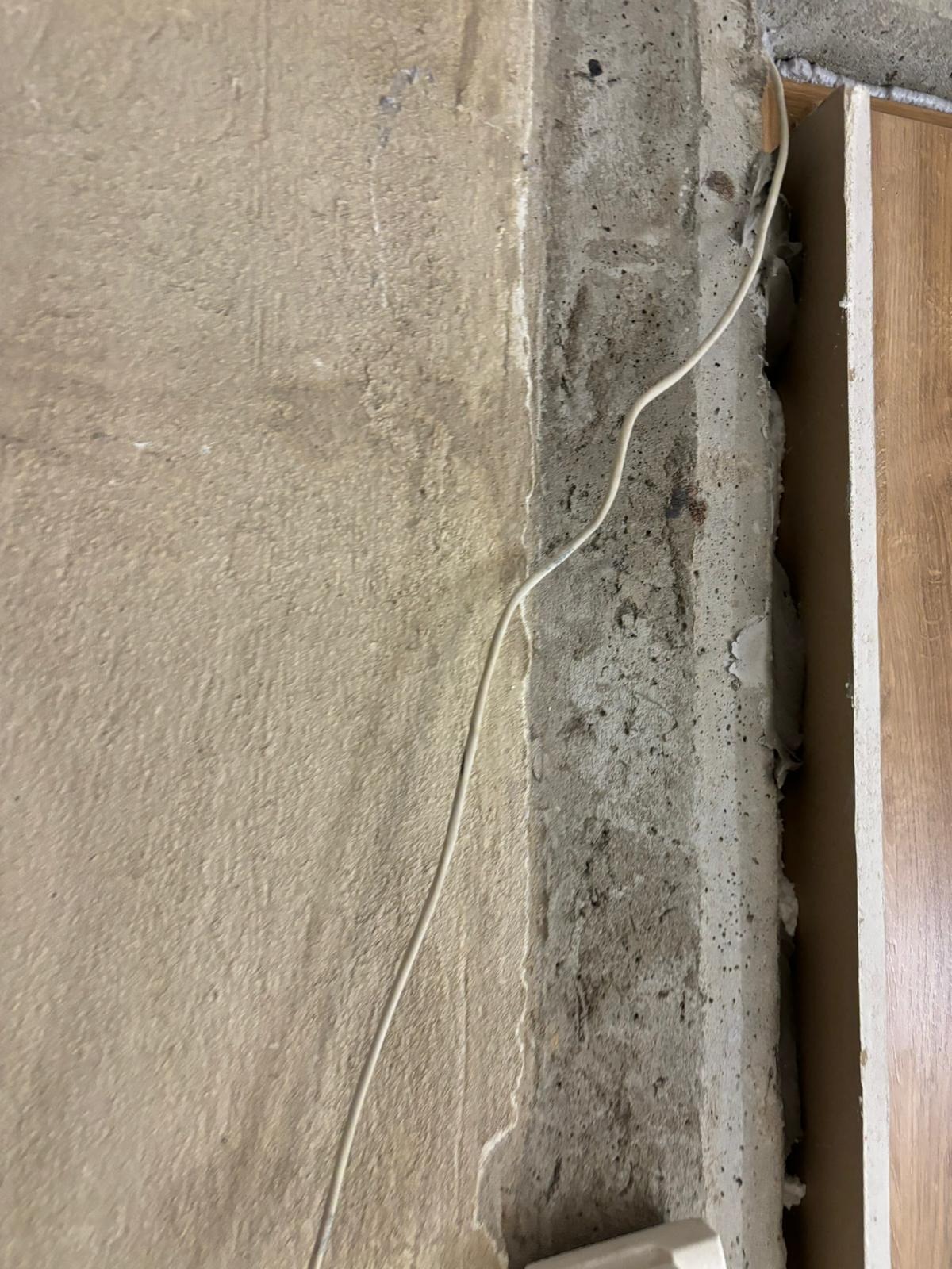 Surowa ściana z widocznym przewodem elektrycznym przed nałożeniem gładzi, fragment ościeżnicy drzwiowej.