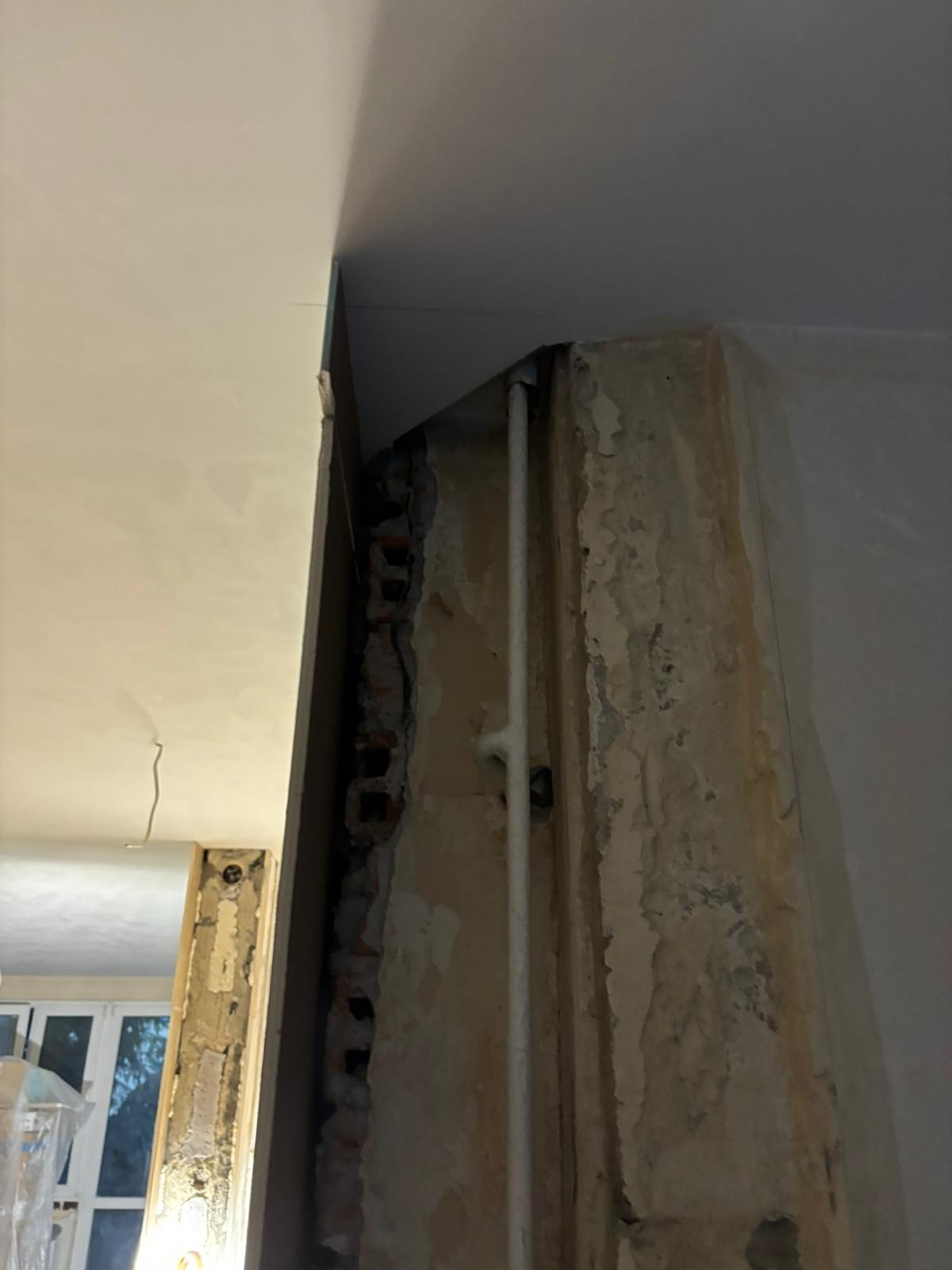 Fragment ściany z odsłoniętą cegłą i instalacją, przygotowanej do nałożenia gładzi, widoczne nierówności i ubytki w tynku.