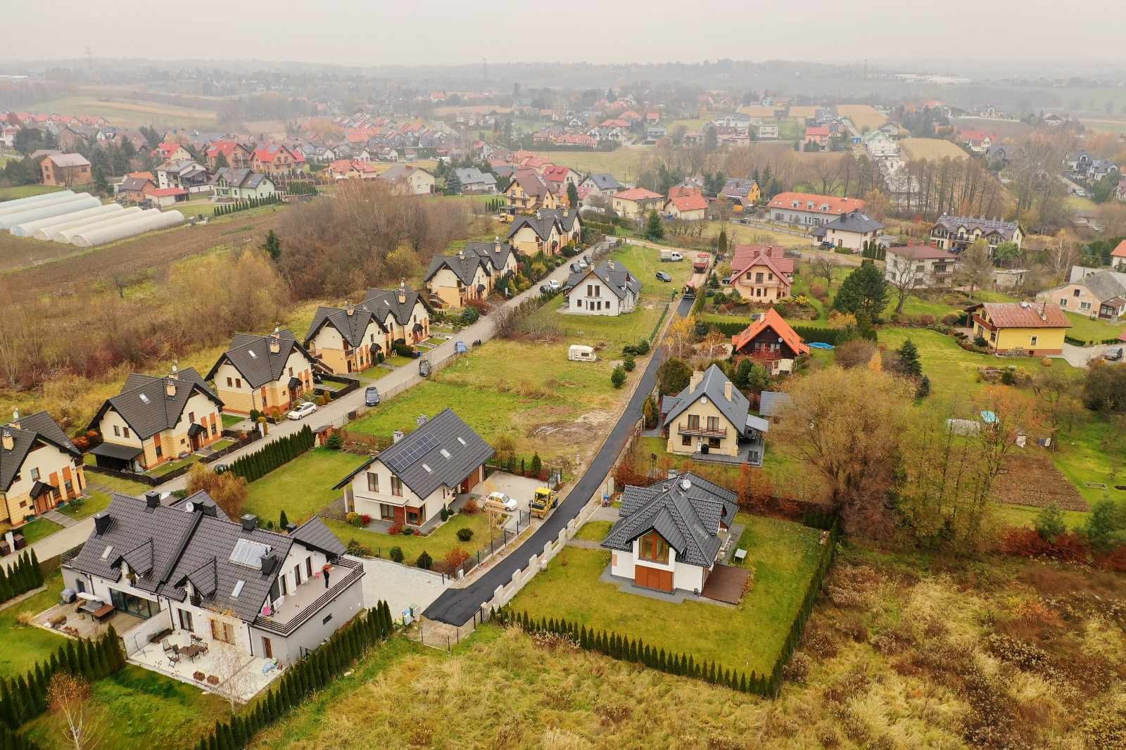 Osiedle domów jednorodzinnych z nową, asfaltową drogą dojazdową, widok z lotu ptaka w pochmurny dzień.
