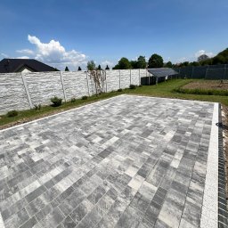 Serhii Molchanov Werolina - Ułożona kostka brukowa w odcieniach szarości na posesji z nowoczesnym ogrodzeniem z paneli imitujących kamień, panele solarne w tle.