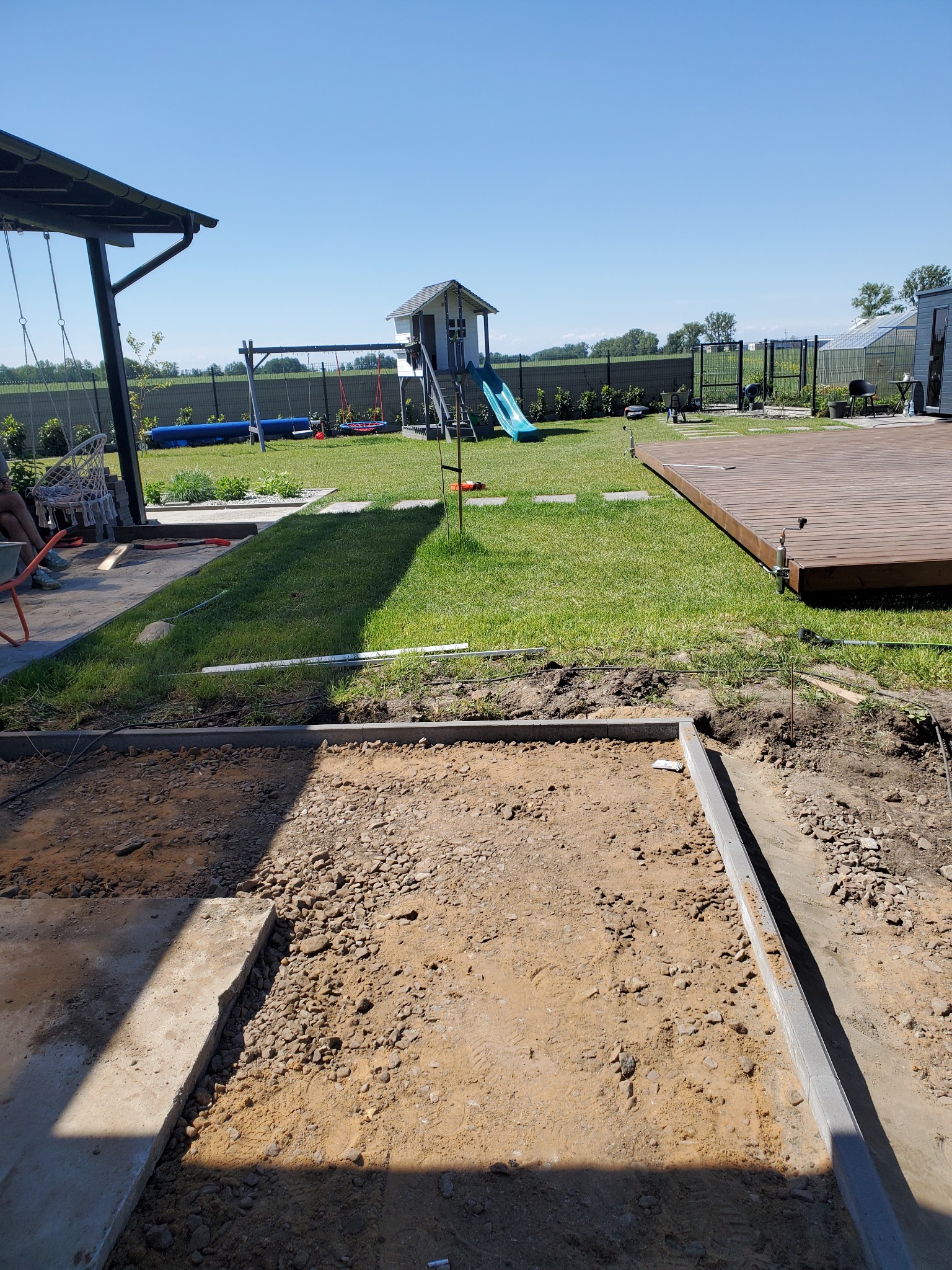 Przygotowany teren pod przyszłą nawierzchnię z obrzeżami, widoczny plac zabaw dla dzieci w tle.