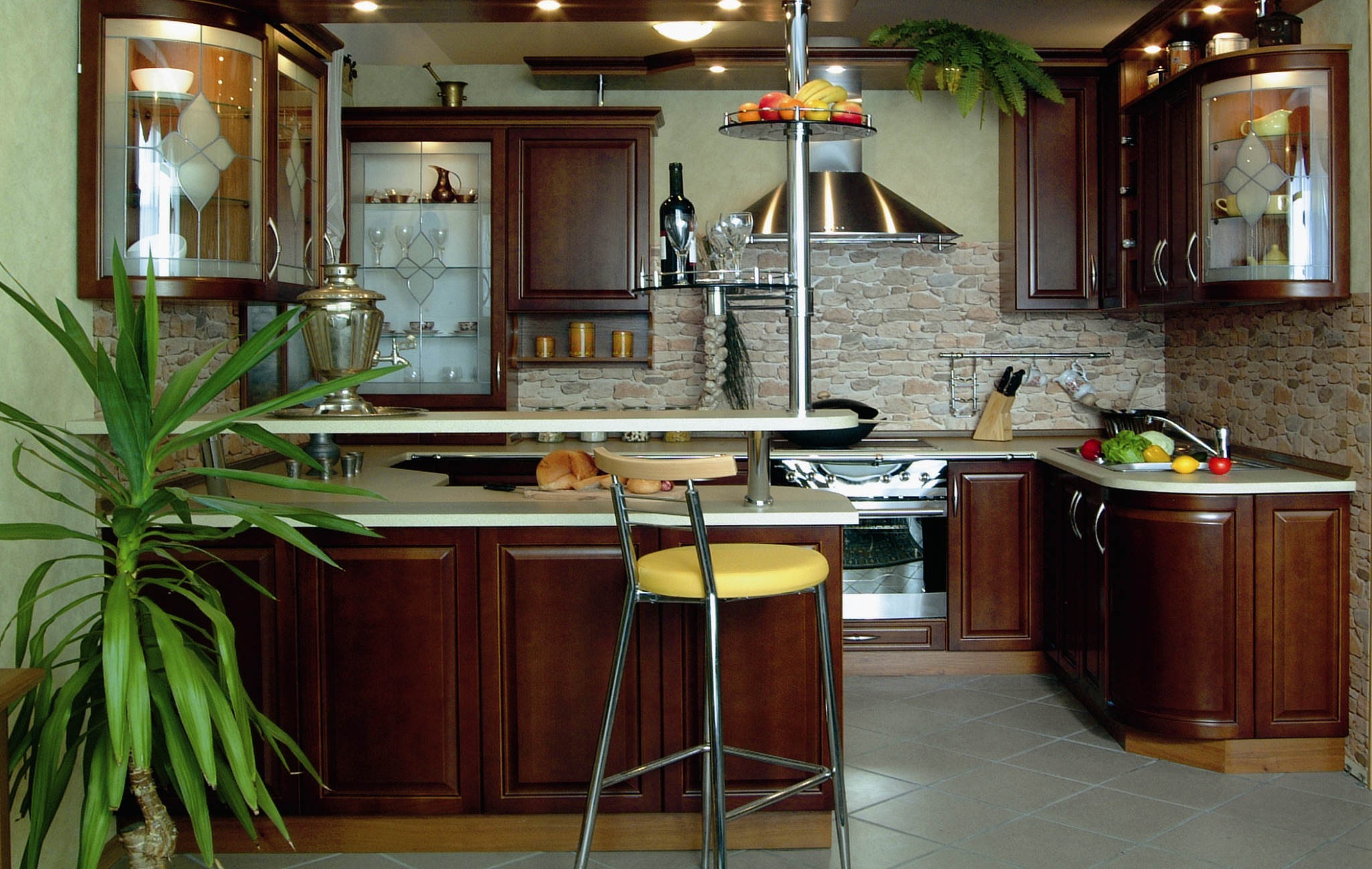 Klasyczna kuchnia z ciemnego drewna, z blatem barowym, rośliną doniczkową i dekoracyjną ścianą z kamienia, oświetlona ciepłym światłem.