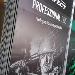 ADMEDIA - Stos wydrukowanych plakatów reklamowych z grafiką przedstawiającą robotnika w kasku i rękawicach, promujących profesjonalną linię produktów.