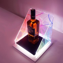 ADMEDIA - Butelka whisky na podświetlonej, geometrycznej ekspozycji z akrylu, z gradientem kolorów, na białym tle.