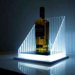 ADMEDIA - Butelka bursztynowego trunku marki Highlander na podświetlonym podeście z pleksi, prezentowana w minimalistycznym studiu.