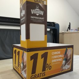 ADMEDIA - Stojak reklamowy marki Vidaron z hasłem '11% gratis' i informacją o impregnacie ochronno-dekoracyjnym do drewna, w tle ploter tnący.