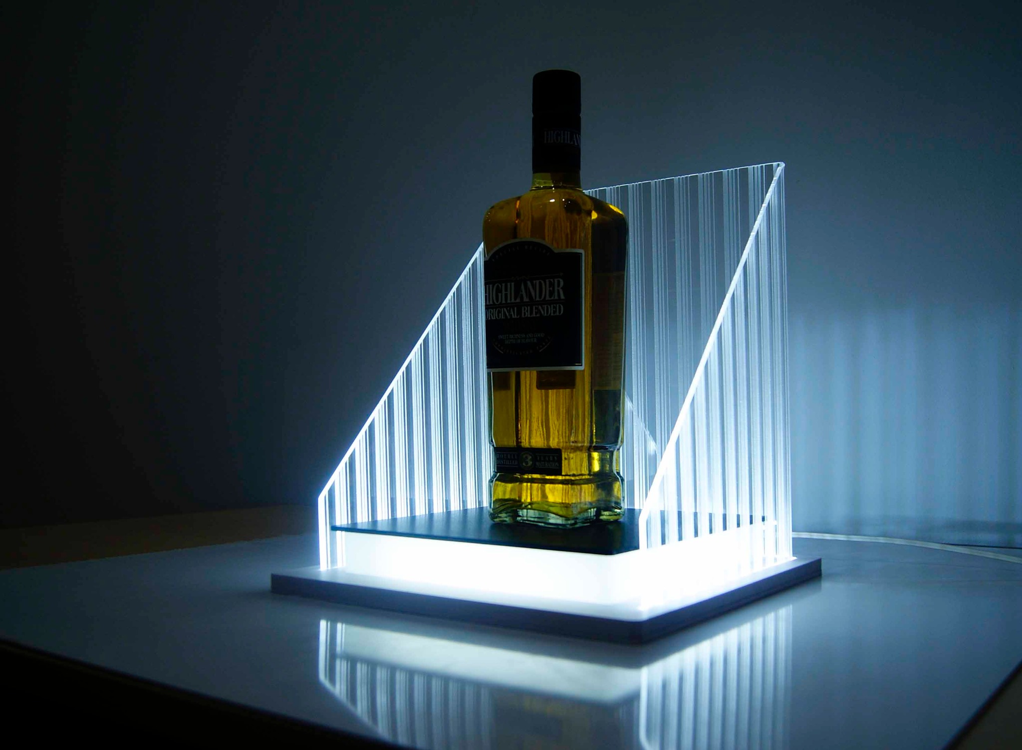 Butelka bursztynowego trunku marki Highlander na podświetlonym podeście z pleksi, prezentowana w minimalistycznym studiu.