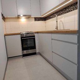 eMCe- Studio - Nowoczesna kuchnia w odcieniach szarości z drewnianym blatem, oświetleniem LED pod szafkami i oryginalną lampą w kształcie gwiazdy.