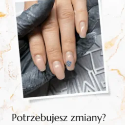 Dłoń z beżowym manicure i niebieskim kwiatowym wzorem na jednym paznokciu, trzymana przez dłoń w czarnej rękawiczce na szarym tle.