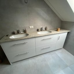 KSmeble Kamil Sławik - Biała szafka łazienkowa z dwoma umywalkami i blatem z jasnego kamienia w łazience na poddaszu z szarą glazurą.