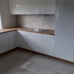 Nowoczesna, biała kuchnia z drewnianym blatem, czarnym zlewozmywakiem i płytą indukcyjną, widok z niskiego kąta, jasne płytki na podłodze.