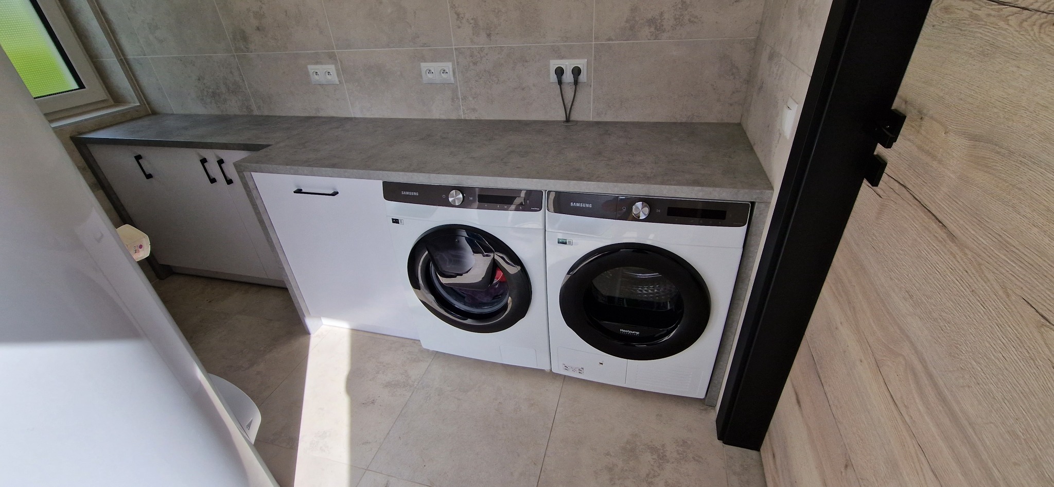 Pralka i suszarka Samsung w zabudowie meblowej z szarym blatem, szare płytki na ścianie, widok z góry.