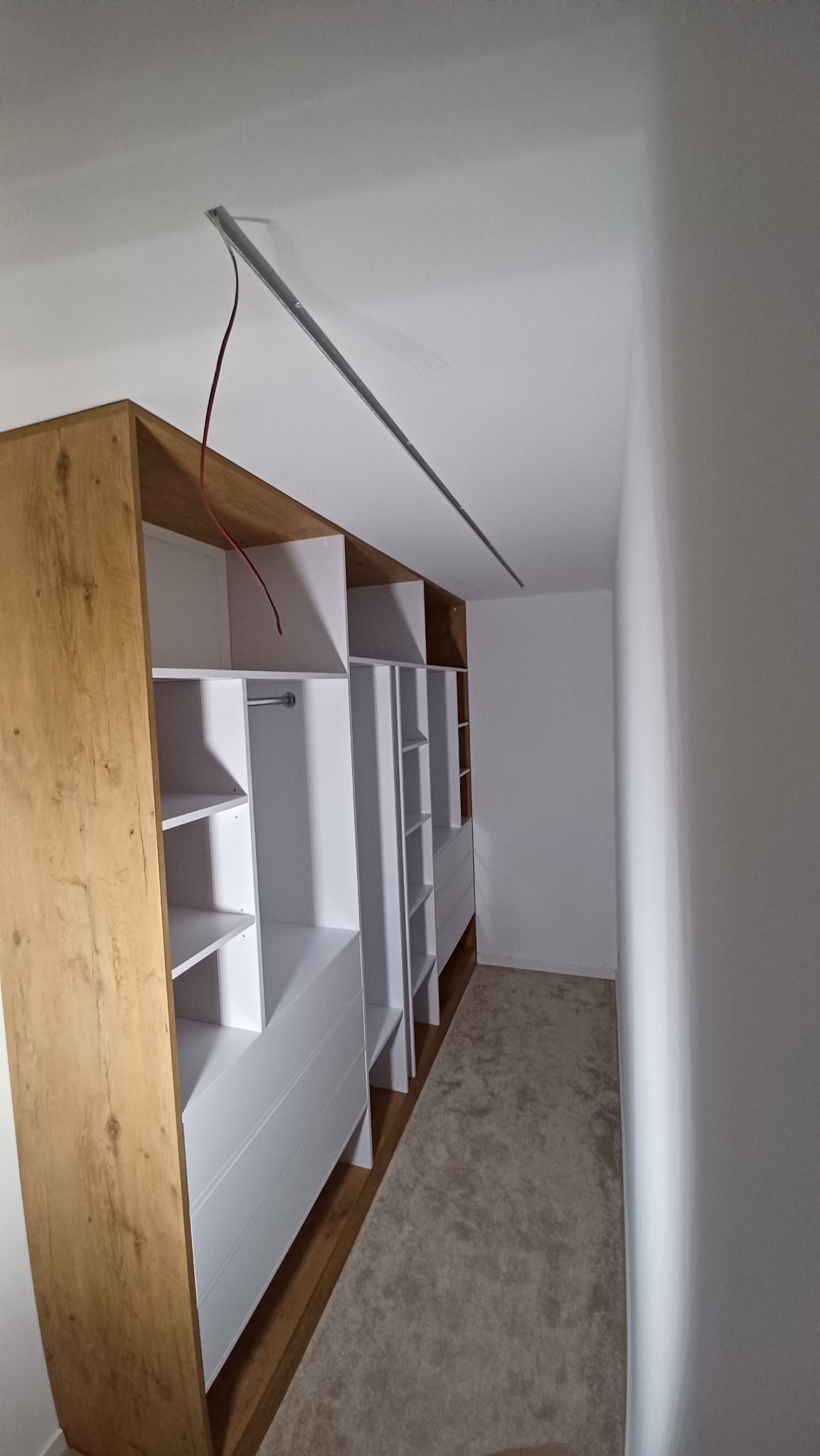 Wnętrze garderoby z szafą wnękową na wymiar, widoczna szyna oświetleniowa na suficie i otwarte półki z szufladami.