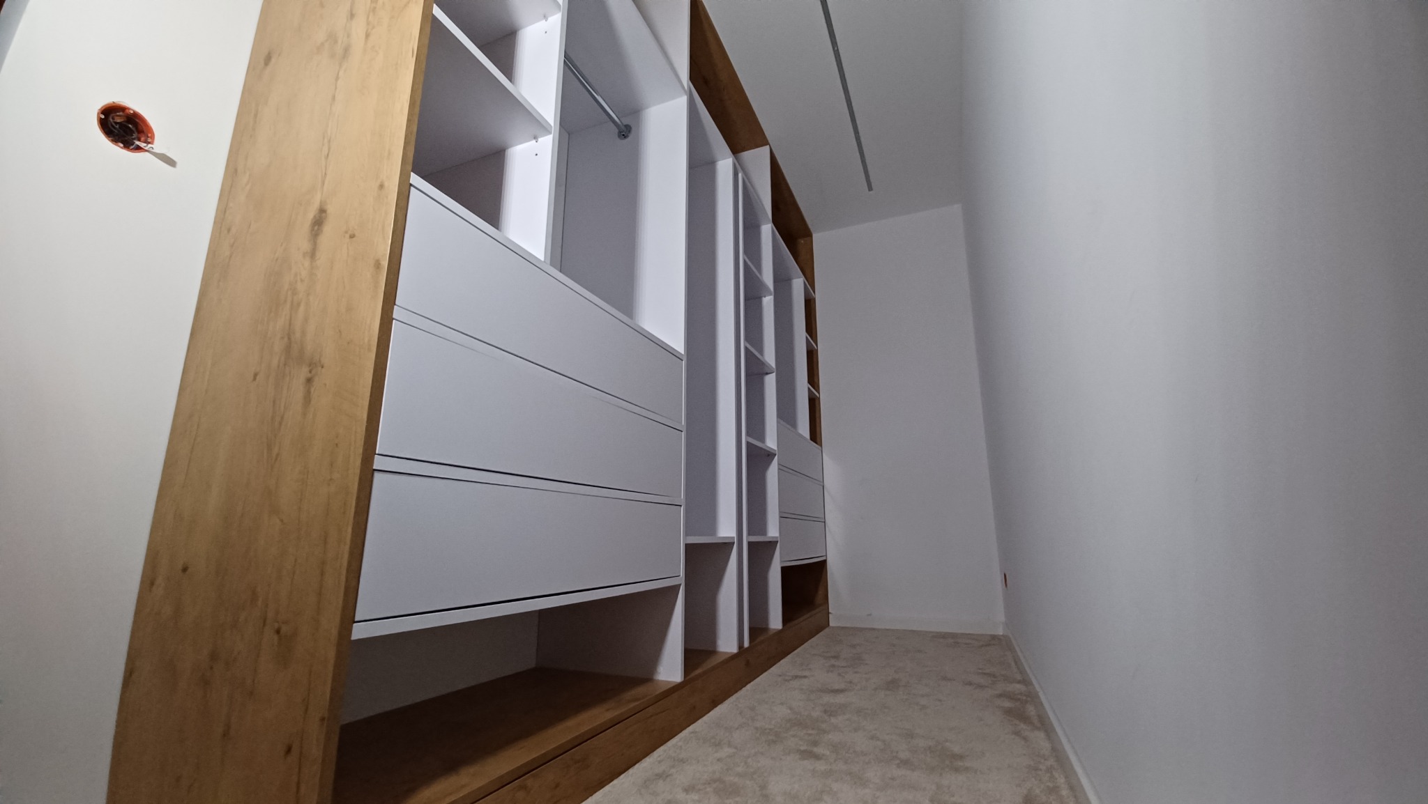 Wnętrze szafy wnękowej z białymi frontami i drewnianymi elementami wykończeniowymi, zrealizowanej w Dzielawach, widok z dołu ukazujący półki i szuflady.