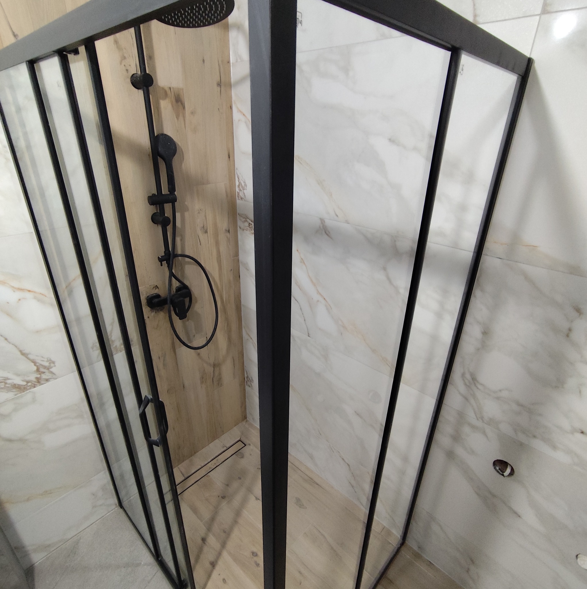 Nowoczesna kabina prysznicowa z czarnymi profilami i deszczownicą, wykończona płytkami imitującymi drewno i marmur w Rabce-Zdroju. Minimalistyczny design.