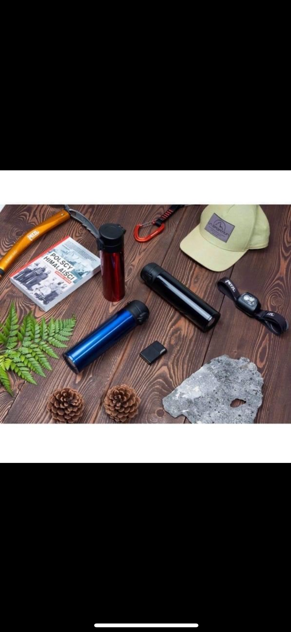 Kompozycja na drewnianym blacie: trzy metalowe termosy (niebieski, czarny, czerwony), czołówka Petzl, książka 'Polscy Himalaiści', karabinek, czapka z logo górskim, skała, dwie szyszki i gałązka...