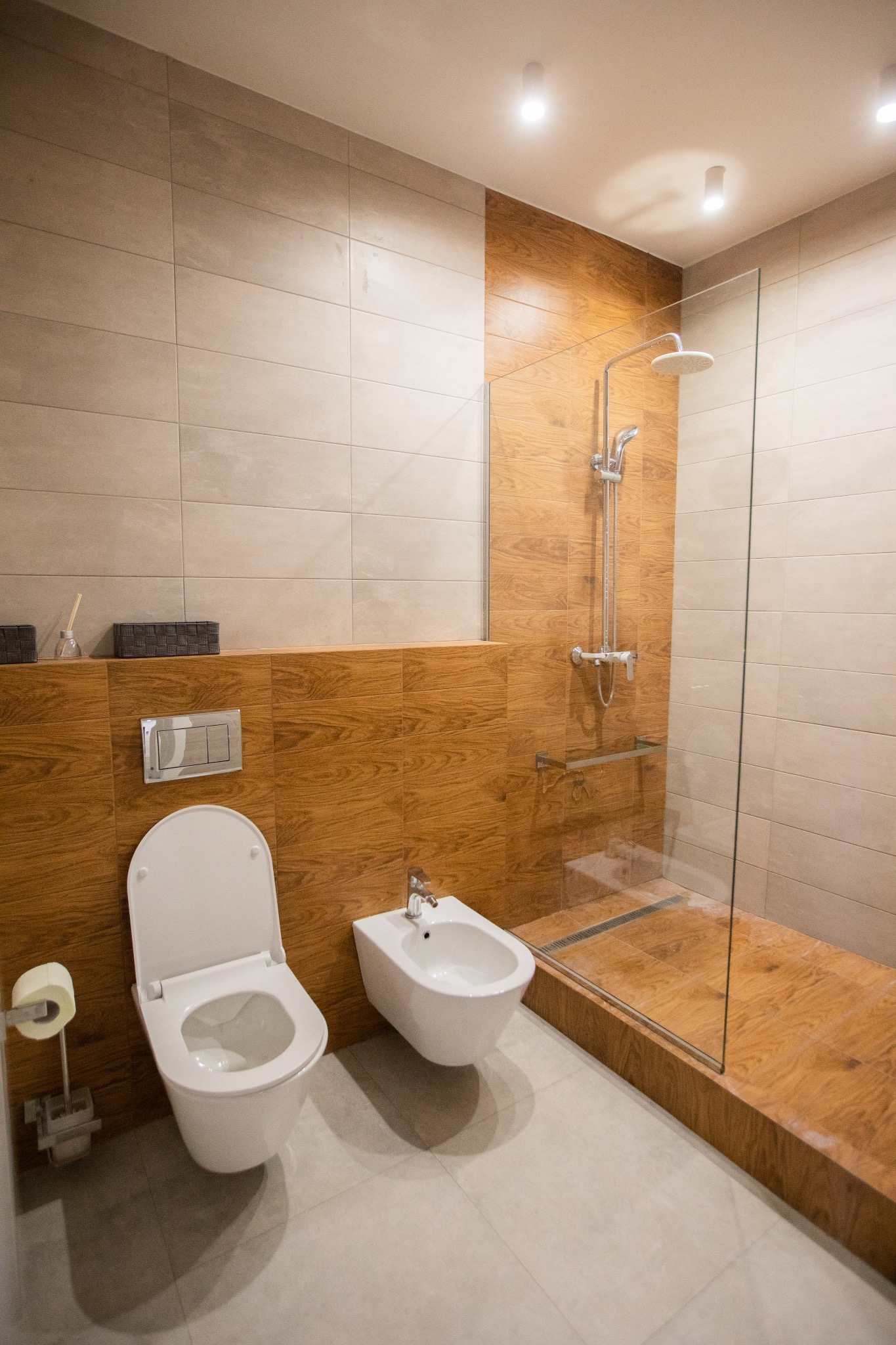 Nowoczesna łazienka z kabiną prysznicową typu walk-in, toaletą i bidetem, wykończona płytkami w odcieniach beżu i drewna.
