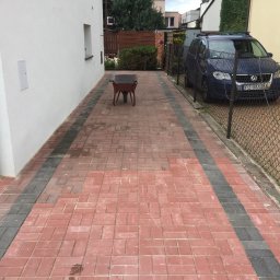 Łucki Garden Bruk - Czerwona kostka brukowa z szarymi pasami, wózek budowlany w perspektywie, auto zaparkowane obok ogrodzenia. Estetyczne wykończenie podjazdu.
