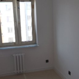 Krzysztof Smoliniec KRIS BUD - Jasne, świeżo pomalowane wnętrze pokoju z oknem i grzejnikiem. Widoczne gładkie ściany, przygotowane do dalszego wykończenia. Minimalistyczny styl, neutralna kolorystyka.