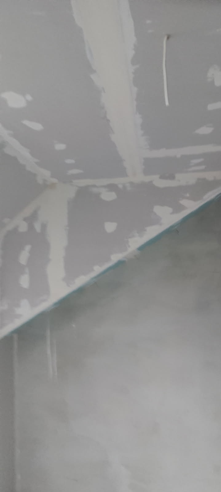 Szpachlowana sufitowa płyta gipsowa z widocznymi łączeniami i fragmentem ściany, przygotowana do dalszych prac wykończeniowych. Widoczne niedoskonałości i nierówności.