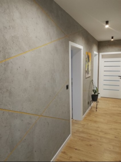 Dekoracyjna ściana w korytarzu z efektem betonu i złotymi liniami w Przędzel. Widoczne drzwi i podłoga z paneli, tworzące nowoczesne wnętrze.