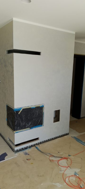 Ściana z wnękami w trakcie wykończenia, zabezpieczona folią i taśmą malarską. Widoczne kable na podłodze i listwa przypodłogowa z oświetleniem LED.