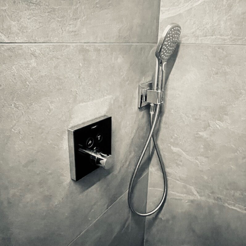 Szara łazienka z chromowaną baterią podtynkową i słuchawką prysznicową na ścianie z imitacją kamienia.