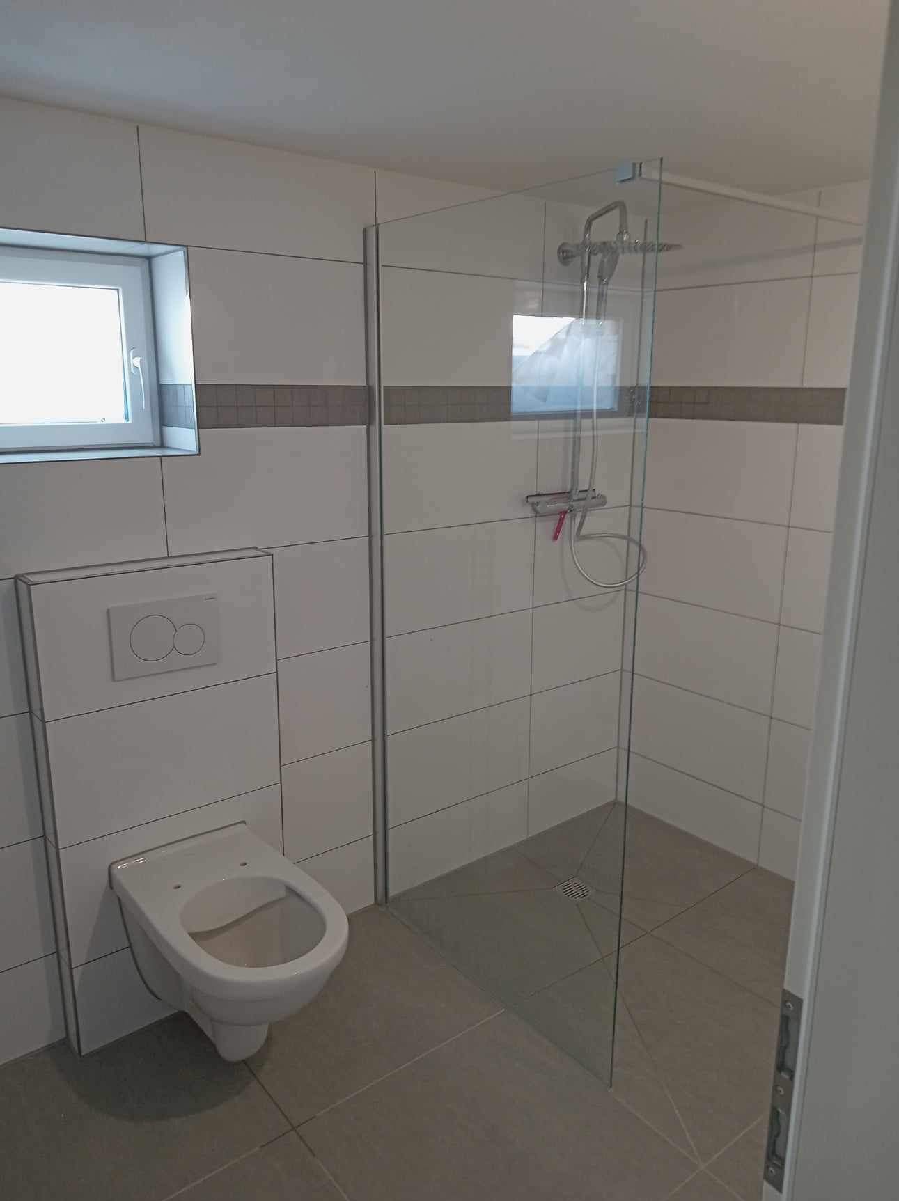 Nowoczesna łazienka z kabiną prysznicową typu walk-in, podwieszanym WC i szarą mozaiką dekoracyjną na białych płytkach.