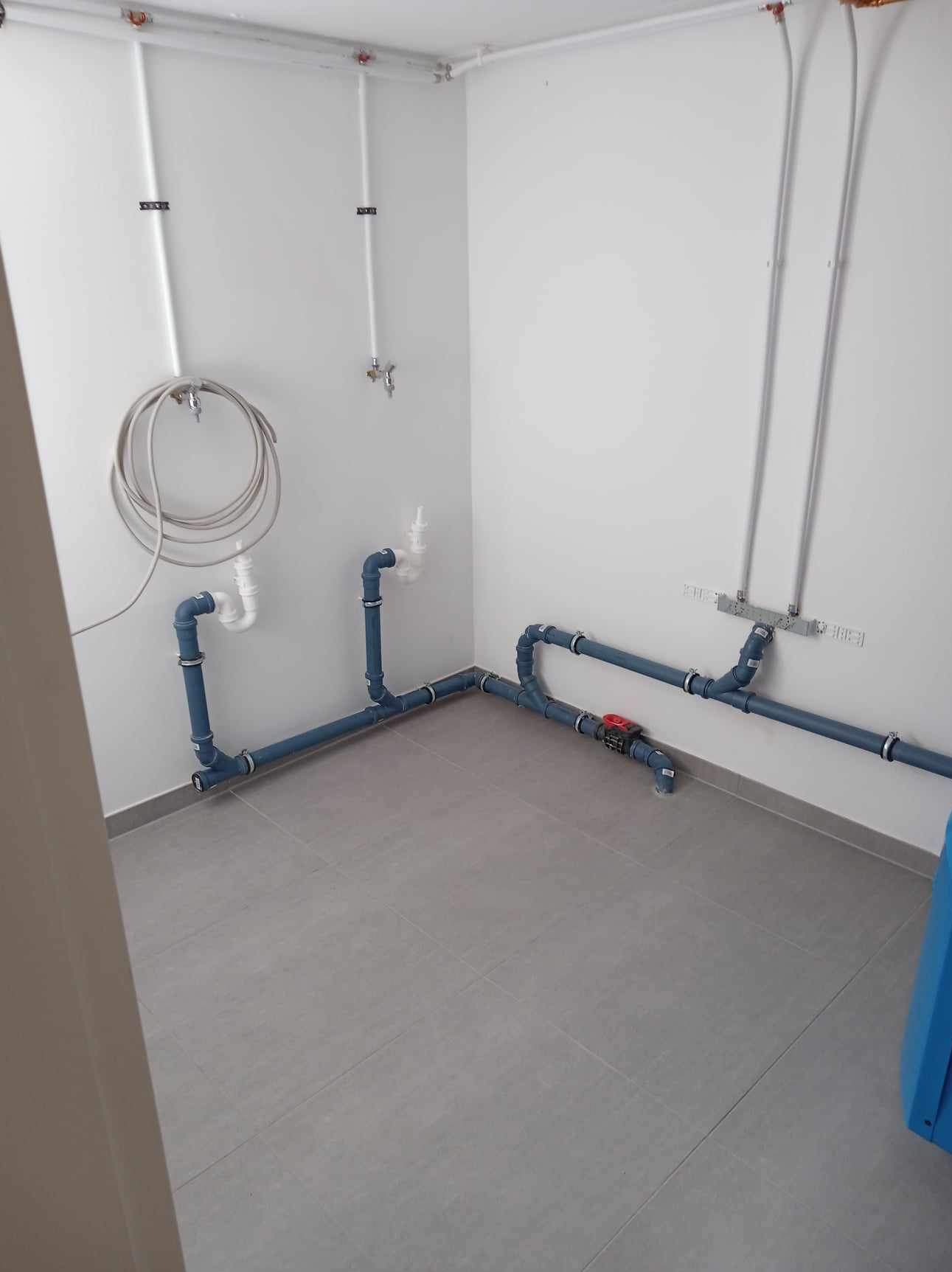 Nowa instalacja wodno-kanalizacyjna z szarych rur w pomieszczeniu z szarą podłogą z płytek, widoczne zawory i przyłącza.