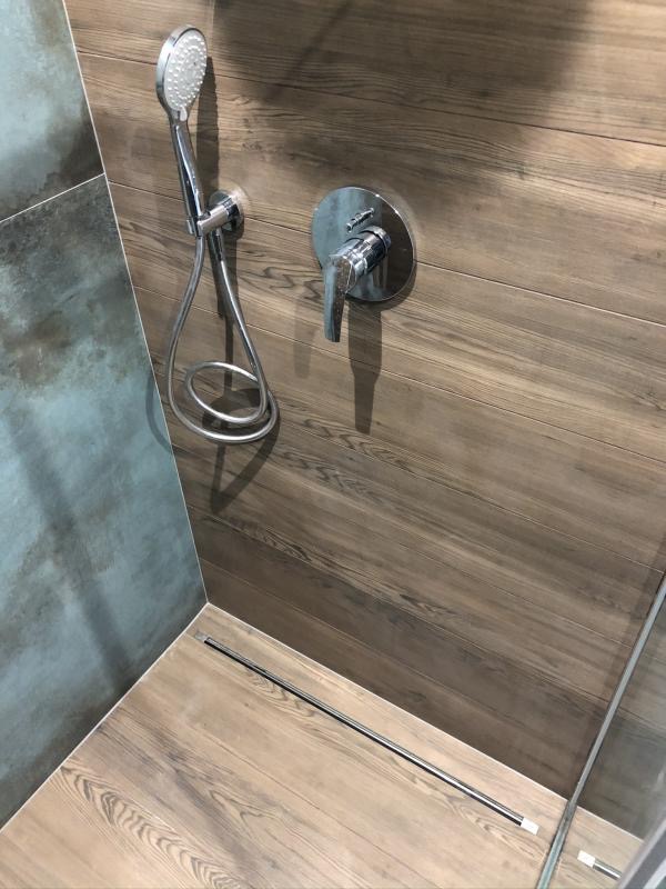 Nowoczesny prysznic z drewnopodobnymi płytkami, chromowaną armaturą i odpływem liniowym w rogu kabiny.