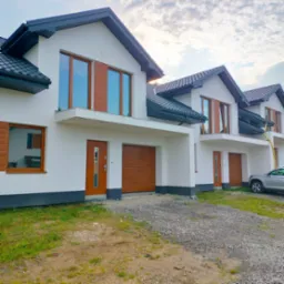 Szereg nowych domów jednorodzinnych z drewnopodobnymi bramami garażowymi i oknami, widok z zewnątrz, częściowo zagospodarowany teren.