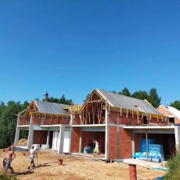 MĘŻYK-BUD MARCIN MĘŻYK - Budowa domu jednorodzinnego w Grybowie: ściany z czerwonej cegły, drewniana konstrukcja dachu w trakcie montażu, widoczni pracownicy budowlani.