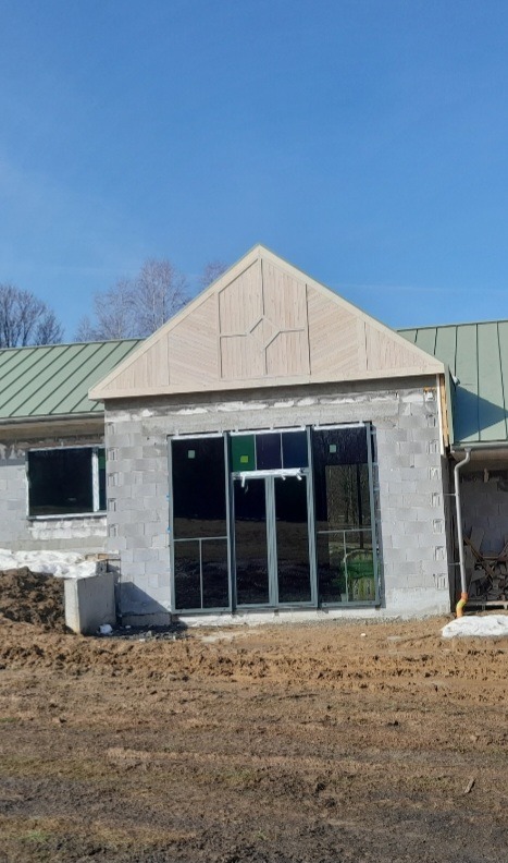 Dom w trakcie rozbudowy: ściany z bloczków, wstawione okna, drewniane wykończenie szczytu dachu, zielony dach, ziemia wokół budynku.