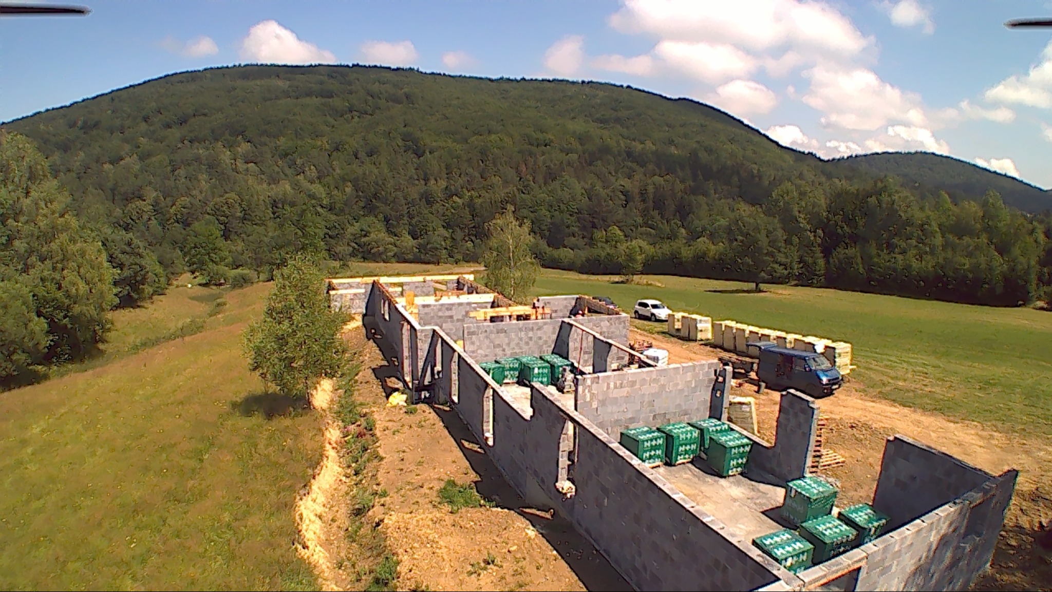 Wznoszone mury parterowego domu z bloczków betonowych na tle zalesionego wzgórza, widok z drona.