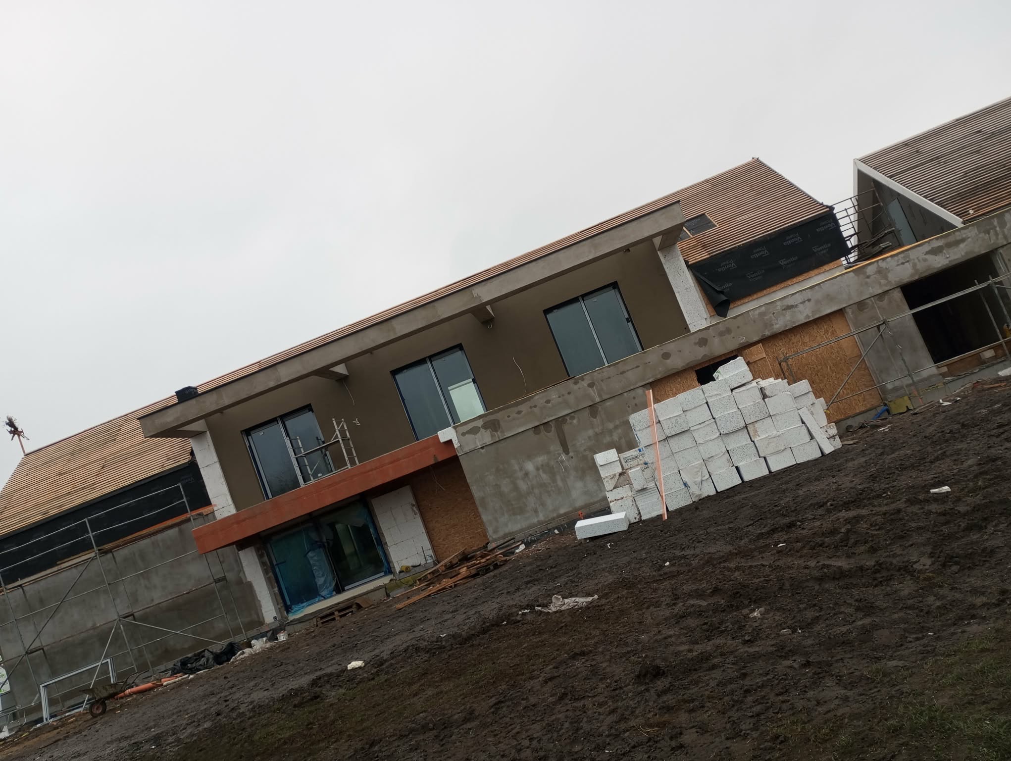 Budowa domu jednorodzinnego w trakcie krycia dachu dachówką ceramiczną. Widoczne rusztowania, bloczki Ytong i folia dachowa.