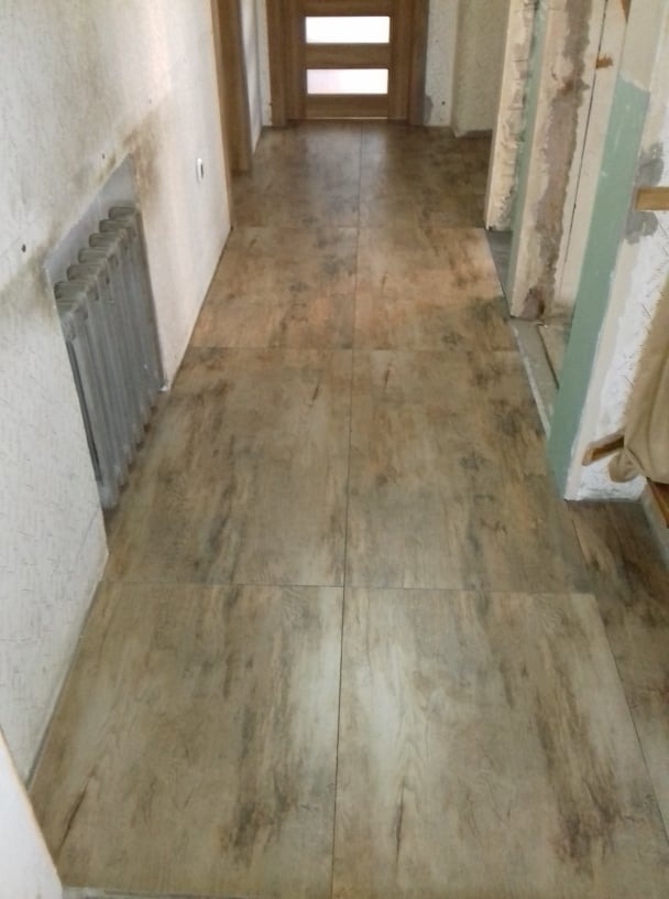 Ułożone płytki podłogowe imitujące drewno w korytarzu podczas remontu; widoczny grzejnik ścienny i surowe ściany w tle.