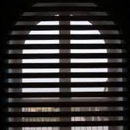 PPHU ROLETY24 ROBERT JAROSŁAWSKI - Zasłonięte okno z widocznymi poziomymi lamelami, tworzącymi efekt światłocienia. Silne oświetlenie z zewnątrz przez okrągłe okno.