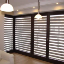 Eleganckie rolety dzień i noc w brązowych ramach okiennych, widoczne z wnętrza pokoju z białym fotelem i drewnianą podłogą, oświetlone lampami sufitowymi.