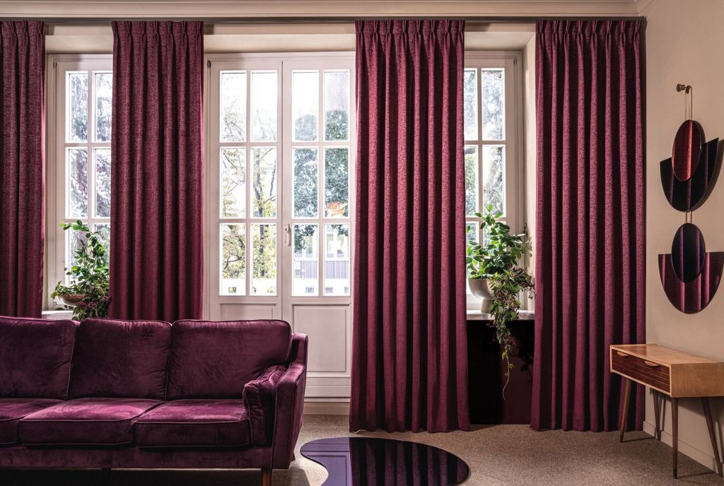 Elegancki salon z bordowymi zasłonami na szynach, dopasowaną sofą z aksamitu i nowoczesnymi dekoracjami ściennymi.