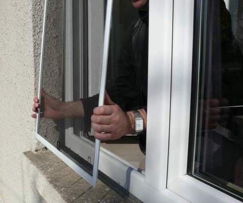 Montaż moskitiery ramkowej w oknie PCV, widoczne dłonie montera i zegarek na ręce.