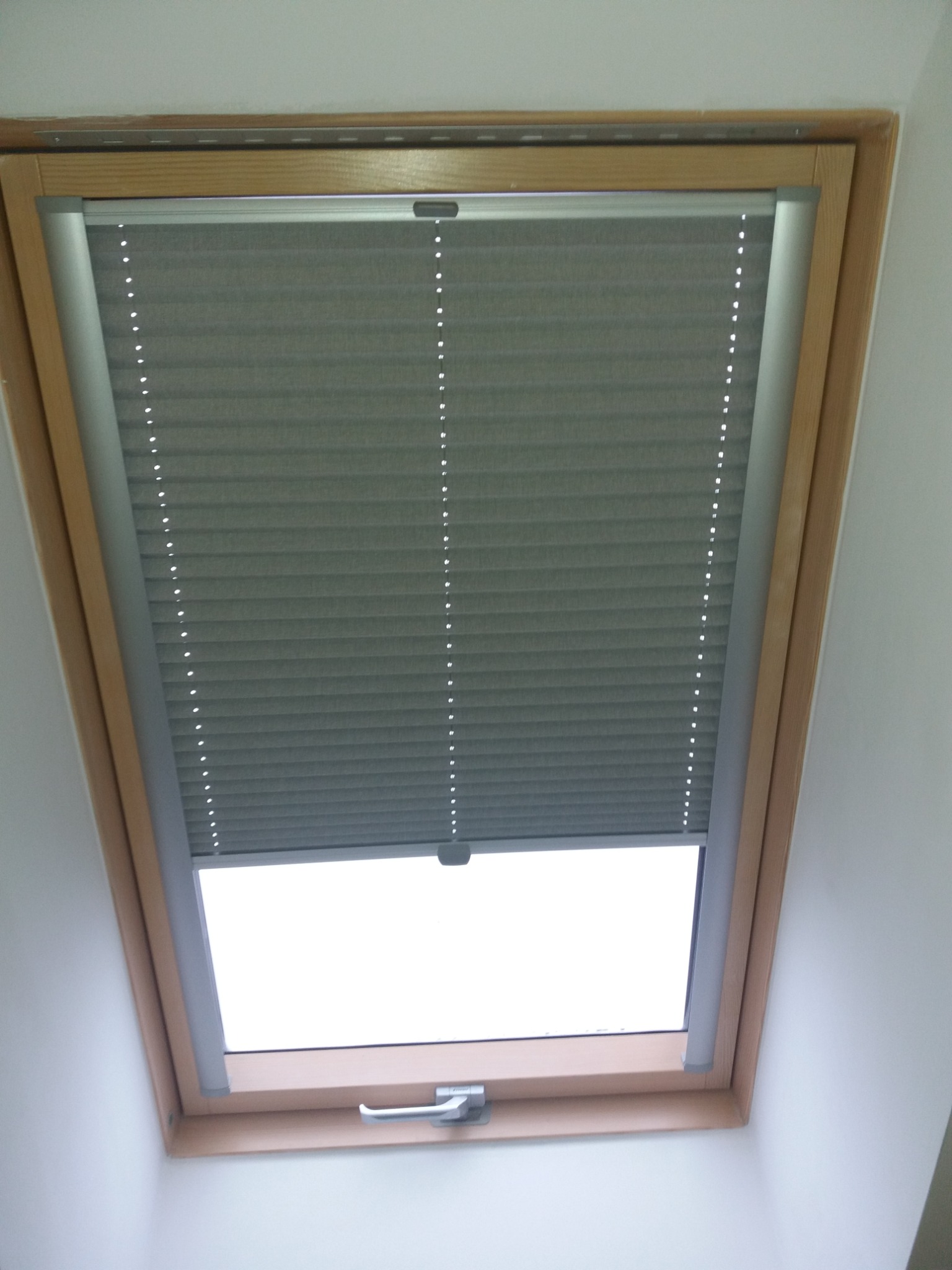 Szara, częściowo rozsunięta przesłona okienna w drewnianej ramie okna dachowego, widok od dołu.