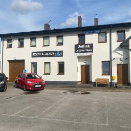 Beata Pająk Ubezpieczenia Jędrzejów UNILINK - Biały budynek z szyldami 'Szkoła Jazdy Plus' i 'Unilink Ubezpieczenia' oraz dwoma samochodami oznaczonymi literą 'L' na parkingu.