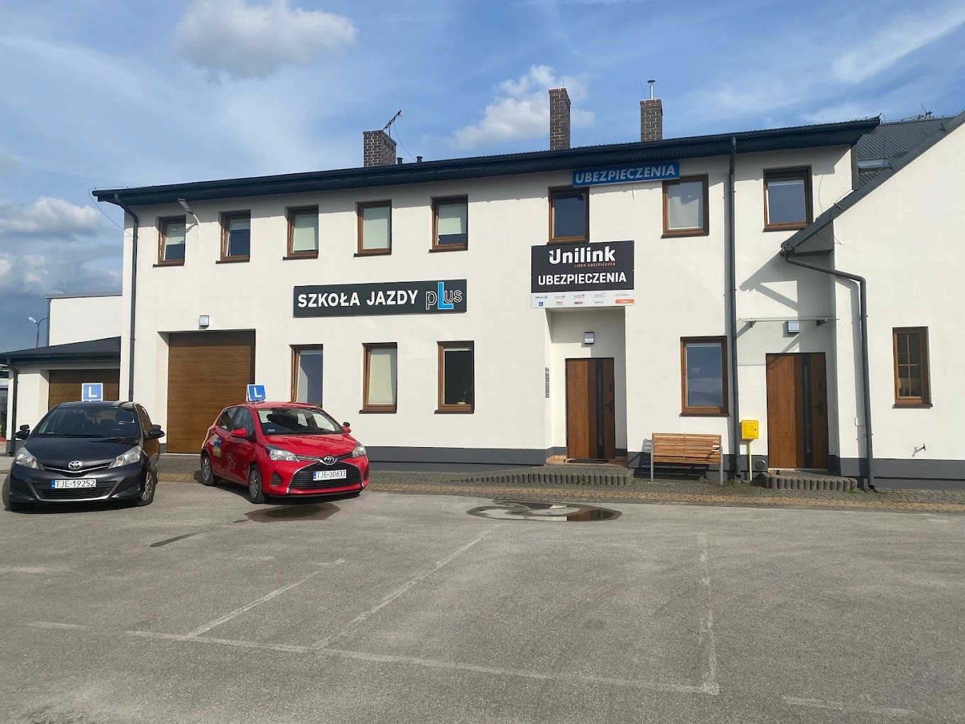 Biały budynek z szyldami 'Szkoła Jazdy Plus' i 'Unilink Ubezpieczenia' oraz dwoma samochodami oznaczonymi literą 'L' na parkingu.