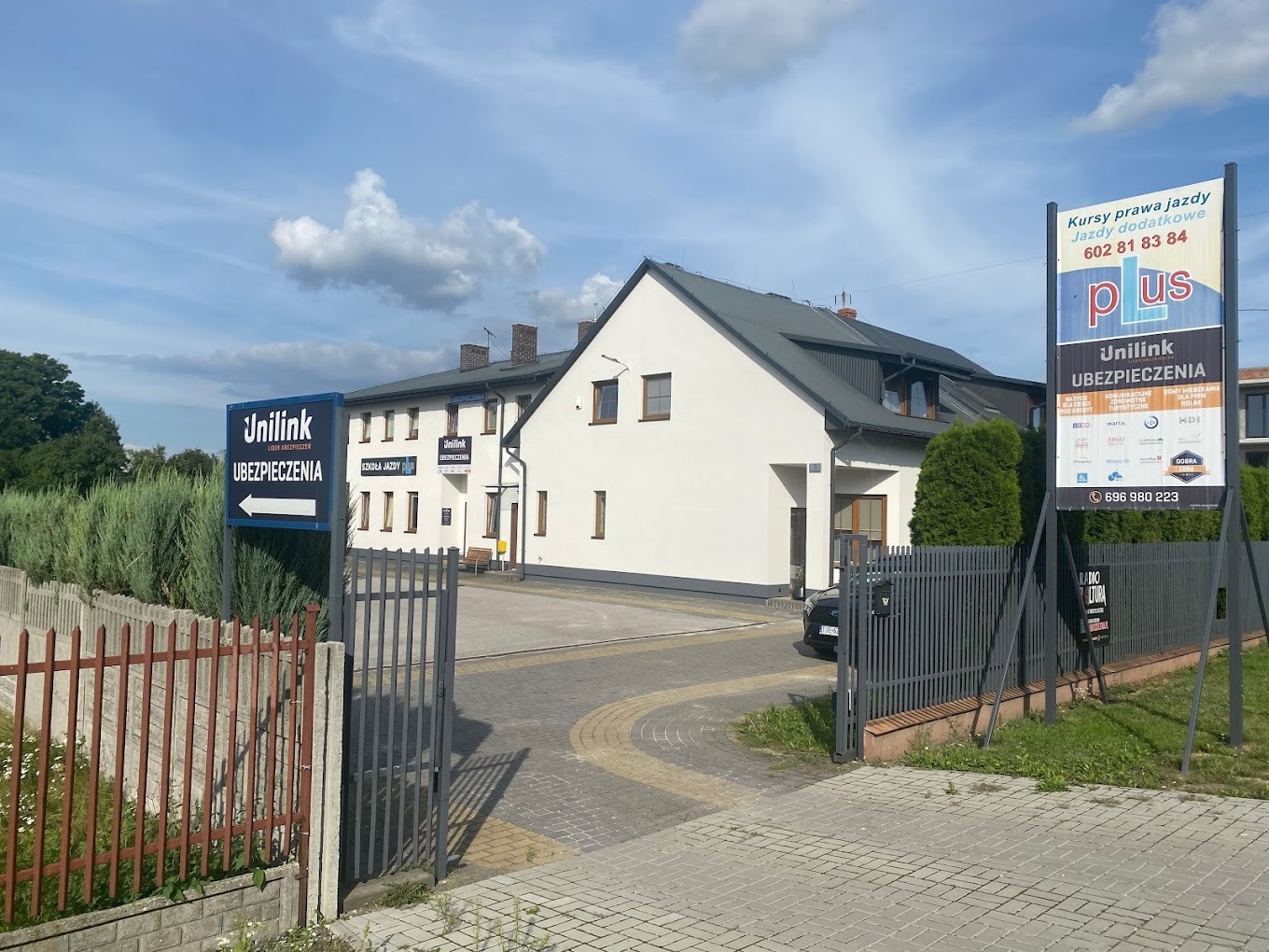 Budynek agencji ubezpieczeniowej Unilink z szyldami informacyjnymi na zewnątrz, widok z ulicy przez metalowe ogrodzenie.