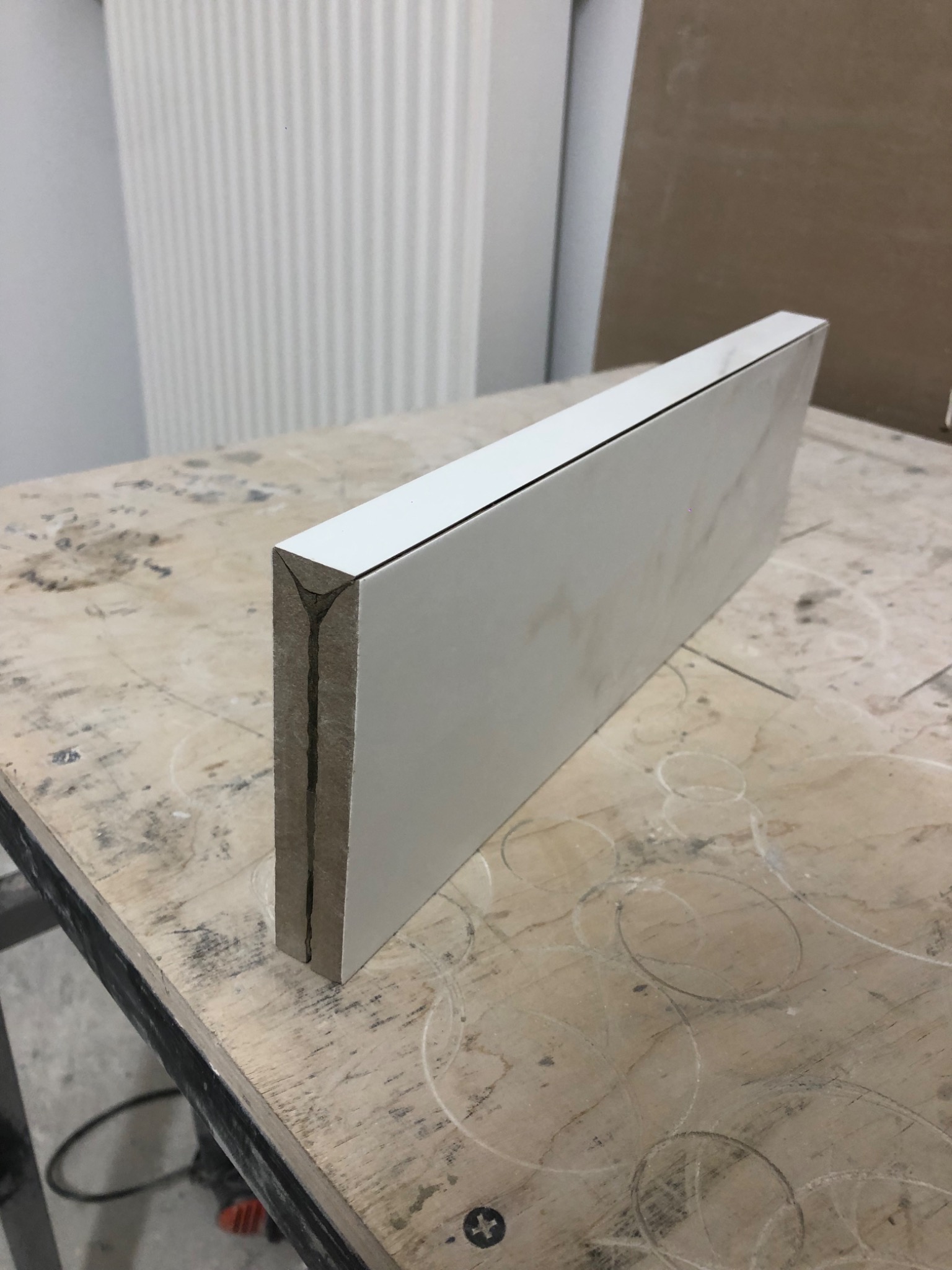 Płytka ceramiczna z białym wykończeniem, widoczny przekrój z fugą, leżąca na brudnym stole roboczym