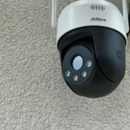 Kamera obrotowa Dahua zamontowana na szorstkiej, jasnej ścianie zewnętrznej budynku, widok z dołu.