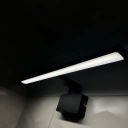 ANVO Patryk Andryszewski - Czarna, nowoczesna lampa LED zamontowana na ścianie z widocznymi śrubami mocującymi obudowę.