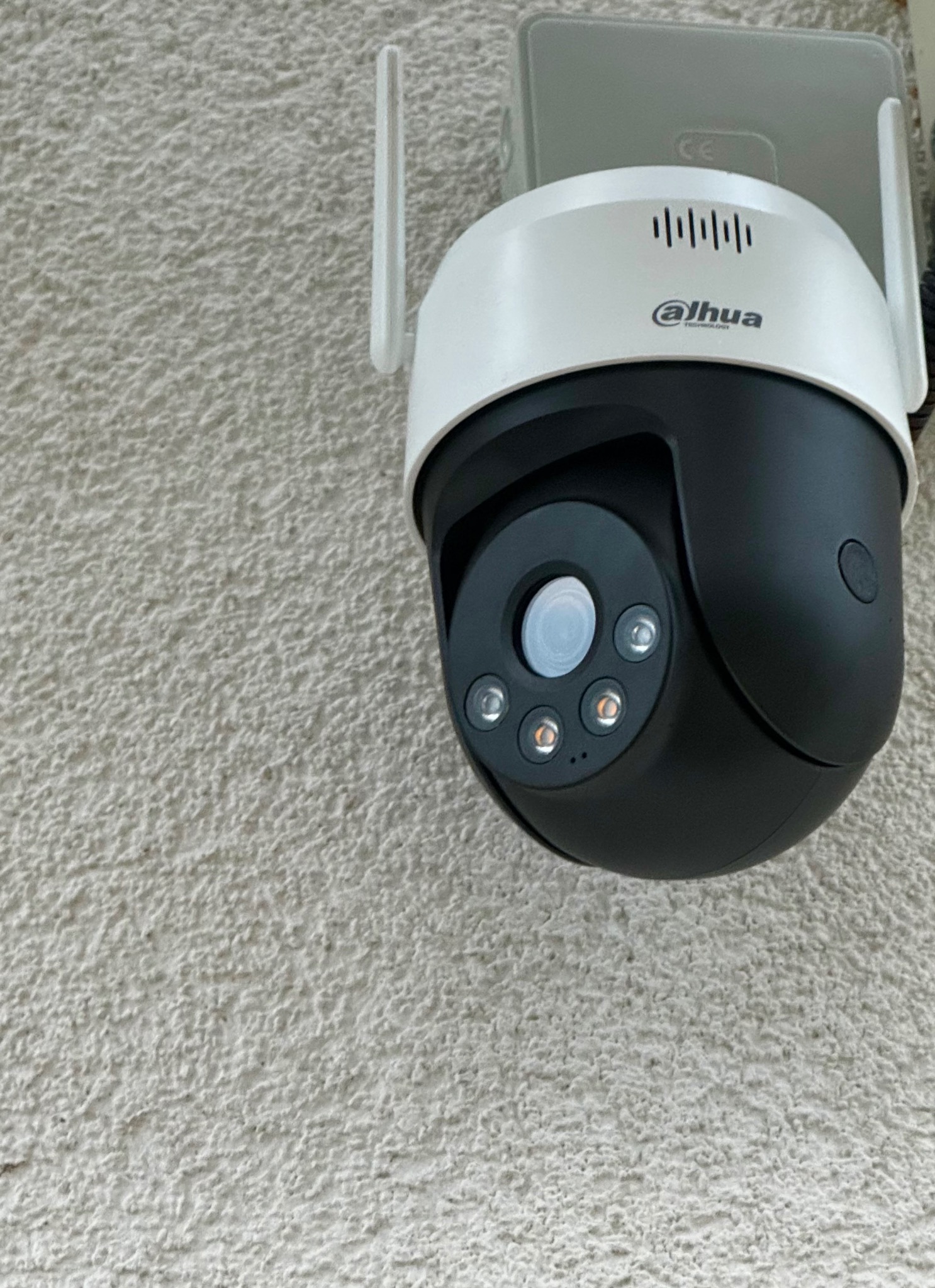 Kamera obrotowa Dahua zamontowana na szorstkiej, jasnej ścianie zewnętrznej budynku, widok z dołu.