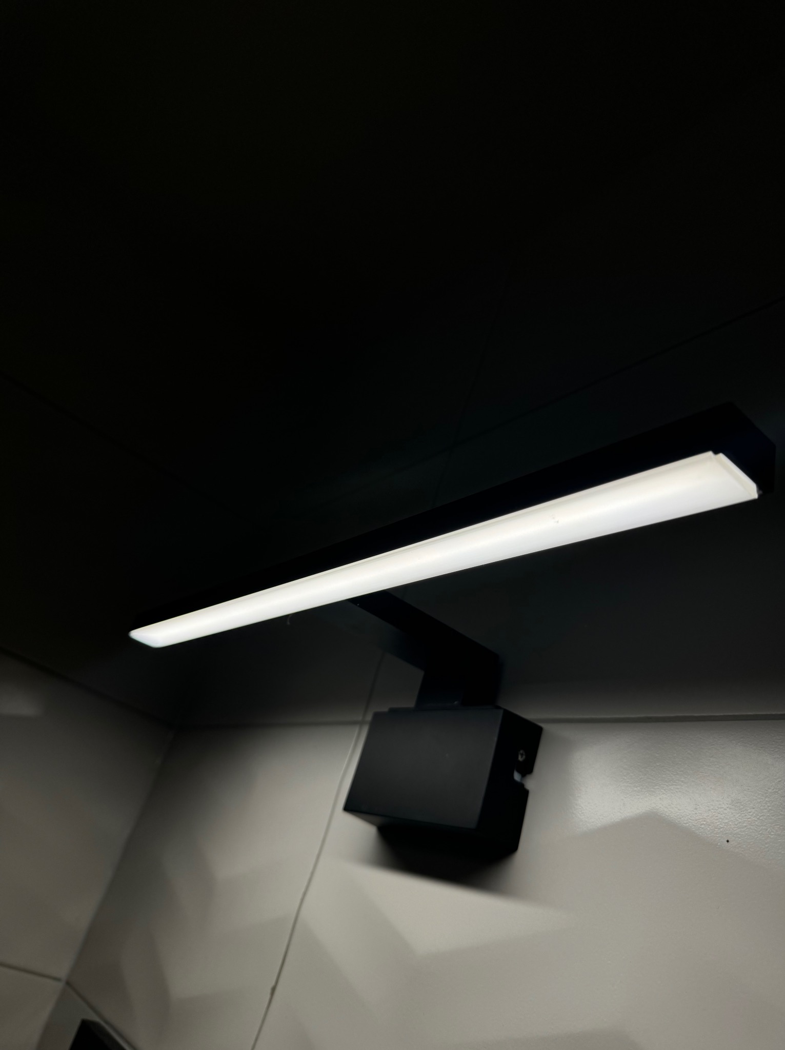 Czarna, nowoczesna lampa LED zamontowana na ścianie z widocznymi śrubami mocującymi obudowę.